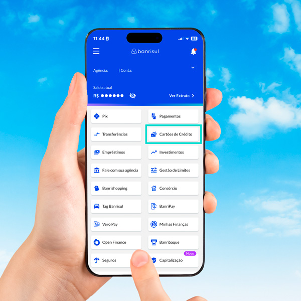 Mão segurando um celular, com a tela de menus do aplicativo Banrisul.